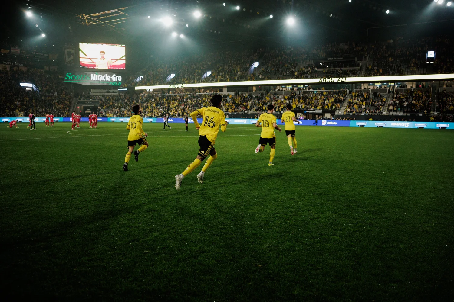 Columbus Crew players jogging across the pitch during a home match, the stands full behind them