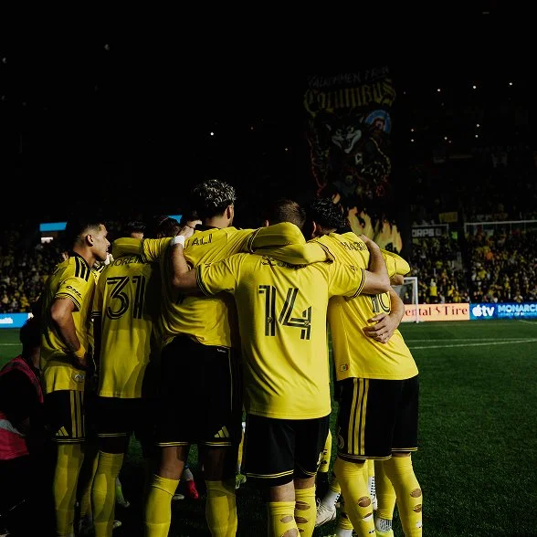 Columbus Crew players in a huddle on the pitch in front of the fans