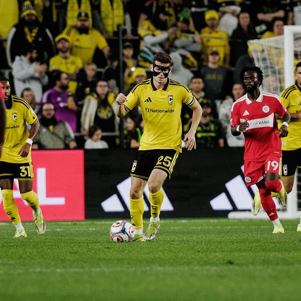 A Columbus Crew player carrying the ball forward with defenders closing in