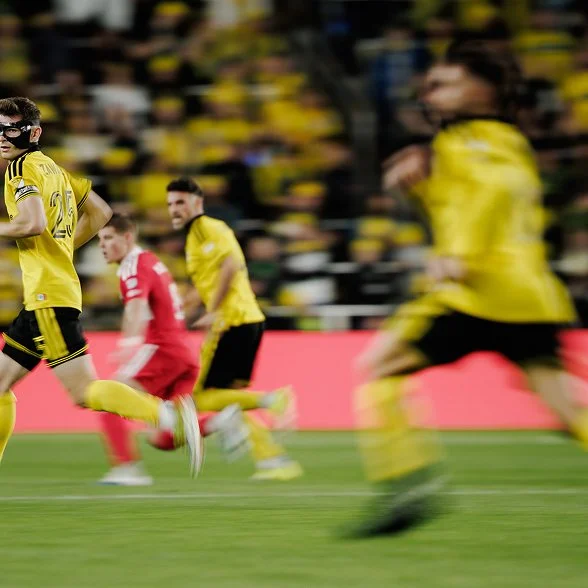 Columbus Crew players sprinting past the camera in a motion-blurred frame