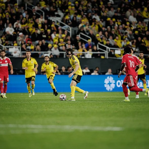 A Columbus Crew player dribbling forward with teammates and opponents around him